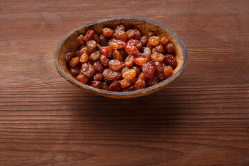 Raisins in a bowl of coconut shell on a wooden table.