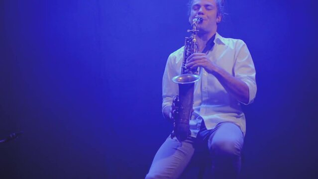 Saxophonist playing his instrument under blue lights, black background. Low angle shot