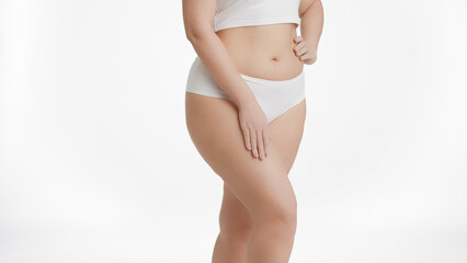 Medium shot of white-skinned plus size woman in white underwear strokes her thigh on white background | Unwanted leg hair removal concept