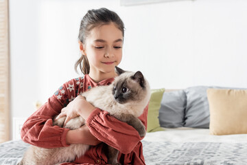 happy girl embracing furry cat at home in bedroom.