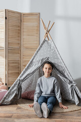 full length view of happy girl sitting on floor in wigwam. © LIGHTFIELD STUDIOS