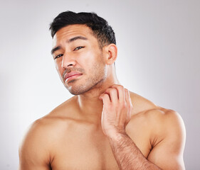 No man escapes ageing. Portrait of a young man checking his skin and looking unhappy during his skincare routine against a grey background.