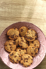 Pink plate filled with chocolate chip cookies on wooden table. Flat lay.