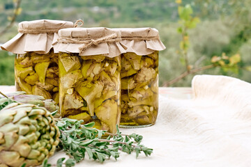 Artichokes hearts marinated with olive oil and herbs. Pickled artichoke in glass jar on the table....