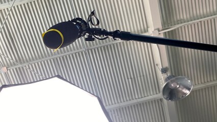 Microphone with windshield, on a boom pole  seen from below, looking up at corrugated metal ceiling and part of a movie light © vesperstock