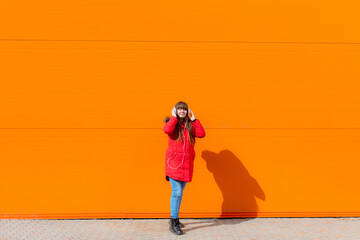 A girl listens to music with headphones on the background of an orange wall . Copy space. Mockup. An article about modern youth. An article about modern music. Article about the choice of headphones.