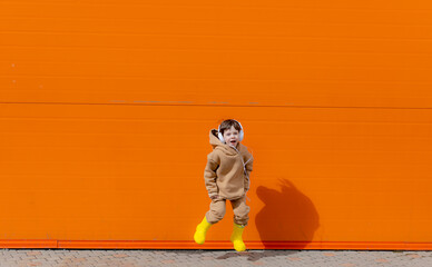 A boy listens to music with headphones on the background of an orange wall . Copy space. Mockup. An article about modern children. An article about modern music. Article about the choice of headphones