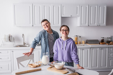 Happy teenagers with down syndrome looking at camera near food in kitchen.