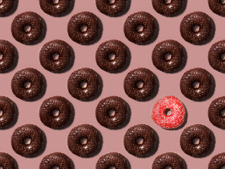 Seamless pattern made with many chocolate and one pink doughnuts on the pastel background. Trendy minimal concept.