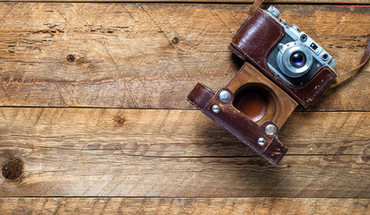 Old vintage camera in leather case on  wooden background from old boards