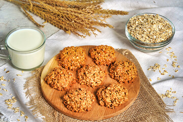 Oatmeal cookies close up view. Stack of homemade delicious rolled oats cookies on table napkin, oat flakes and milk bottle. Morning breakfast table background.