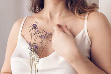 Young woman in a light silk dress with thin straps holding a sprig of lilac gypsophila in her hands.Hands close-up.Spring,awakening of nature concept.Beauty and tenderness concept.