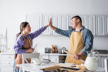 Positive friends with down syndrome giving high five near food in kitchen.