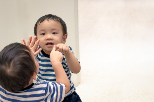 Portrait Of Happy Asian Boy Smile While Pointing His Finger Into His Reflection In The Mirror.