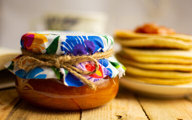 Śniadanie pomarańczowy dżem brzoskwiniowy z ozdobnym wieczkiem, kolorowym materiałem i sznurkiem jutowym oraz naleśniki pancakes i filiżanka