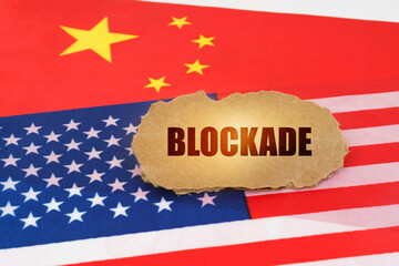 On the flags of the USA and China lies a cardboard sign with the inscription - Blockade