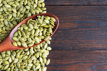 Pumpkin seeds in a wooden spoon on a wooden background. Healthy food. Scattered seeds of pumpkin. Copy space. Flat lay