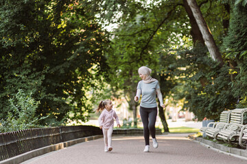 Family sports and outdoor activity concept. Cheerful young Muslim mother in hijab enjoying jogging together in park with her cute active little daughter. Mom and child jogging in the park