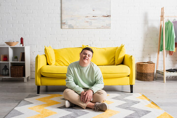 Fototapeta premium Positive teenager with down syndrome sitting on floor at home.