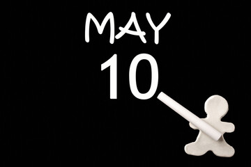 A small white plasticine man writing the date 10 May on a black board. Business concept. Education concept.