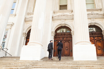 A well dressed man and woman look at each other as they walk up steps of a legal or municipal building in discussion. Could be business or legal professionals or lawyer and client.