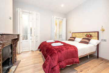Bedroom with wooden bed with wine red duvet and vintage marble fireplace