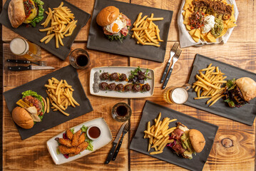 Set of fast food dishes and assorted beef burgers, meatballs with cream cheese, phyto eggs, nachos with guacamole, chicken fingers on wooden table