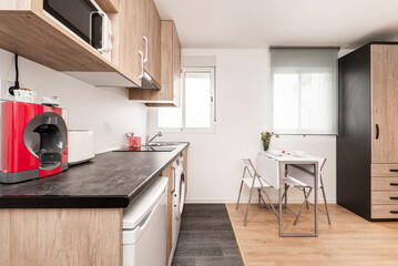 Obraz premium Kitchen with dark gray wood countertops with wood cabinets and white appliances in a study with a white folding dining table and matching chairs