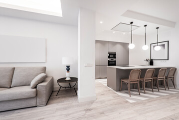 kitchen with white stone countertops, gray cabinets, stainless steel appliances, matching island and living room with sofa upholstered in gray fabric