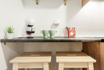 Kitchen with dark gray wooden countertops with cups of coffee and a capsule coffee machine and wooden stools under the counter