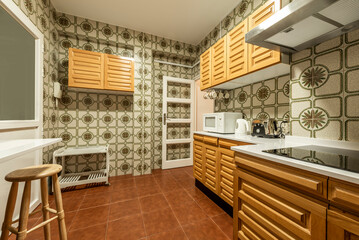 Kitchen with white stone countertops, solid wood furniture and old tiles on the walls, white aluminum door, wooden stool and small appliances on the counter