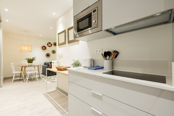 Kitchen with white stone countertops, gloss gray wood cabinets, light wood floors, and dining table with white wood chairs in the background