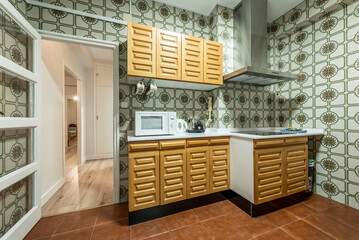 Kitchen with white stone countertops, solid wood cabinets and antique tiles on the walls, wooden door with glass cabinet leading to a white hallway and stainless steel extractor hood