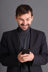 A smiling man in a jacket holds a cell phone in his hands