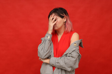 The upset girl covered her face with her hand while standing on a red background