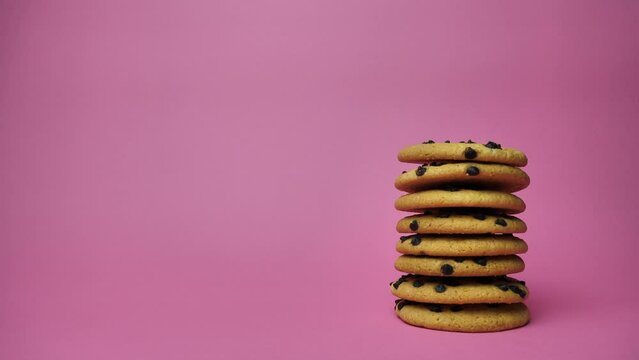 A stack of chocolate chip cookies sprouting on a pink background. American Cookies.place for text