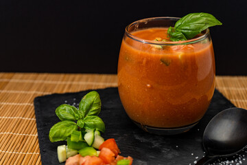 Important Glass with the refreshing Andalusian Gazpacho on a black slab on a mat. A cold vegetable and organic soup or drink that is drunk in summer or hot days. Lower view.
