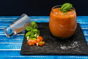 Important Glass with the refreshing Andalusian Gazpacho on a blue wooden table and an empty shot dropped on the side. A cold vegetable and organic soup or drink that is drunk in summer or hot days.