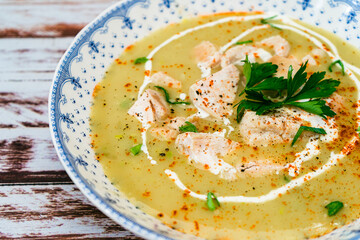 Exquisite dish with a homemade cream of poultry soup with chicken pieces, parsley and cream on a rustic or country style wooden table. Natural and simple food concept. High view