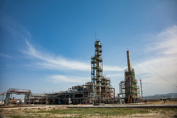 Fototapeta na wymiar Grey distillation tower (refinery column) on blue sky with clouds and mountains. Oil refinery plant in desert near Taraz city, Kazakhstan.