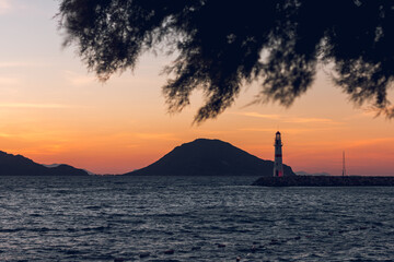 Beautiful sunset view and lighthouse in Turgutreis, Bodrum, Turkey. Red and white lighthouse. In the foreground is a fir branch.