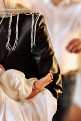 Baptism ceremony of a baby. Close up of tiny baby feet, the sacrament of baptism. The godfather holds the child in his arms. small legs of a newborn baby