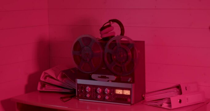 Red light of the night room. Tape reels spin on an old tape recorder. Headphones are on the device. There are documents on the table, the work of the criminal service.