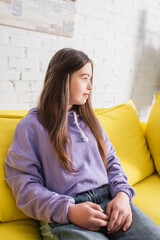 Side view of teen girl with down syndrome sitting on couch at home.