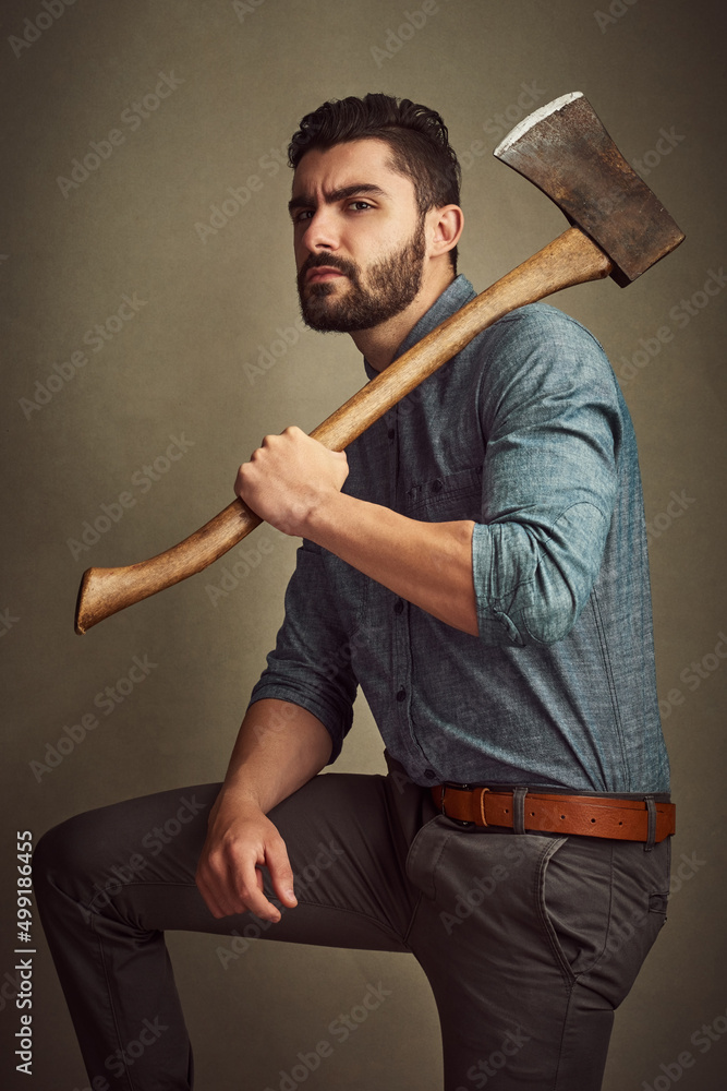 Poster fashionable with the right amount of rugged. studio shot of a young man posing with an axe against a