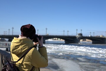 A man photographs the river and the bridge. Ice drift on the river. Spring weather in the city....