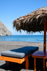 Sun beds and a sun umbrella at the famous black sandy beach of Perissa in Santorini