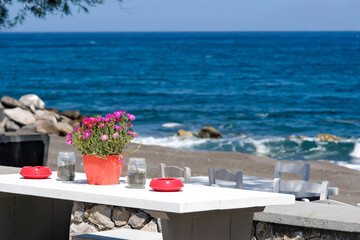 A beautiful outdoor bar decorated with flowers and ashtrays with an amazing view of the famous beach of Perissa in Santorini