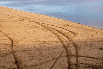 Tire tracks on the sand of an empty beach near the river