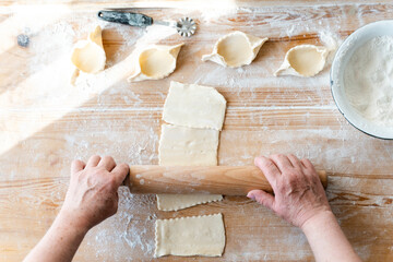Woman using roller pin while making bakery from dough at the wooden table